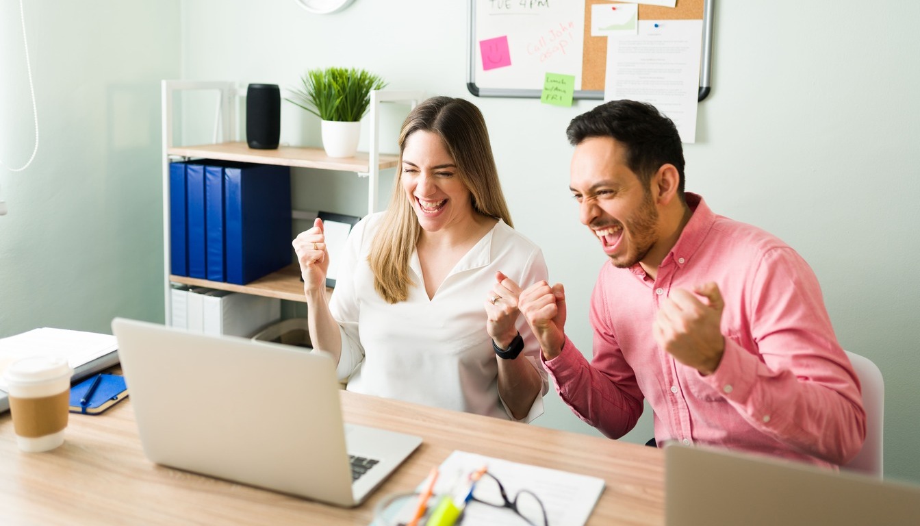 colegas profesionales celebrando emocionados durante videollamada en oficina